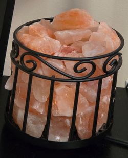 Cylindrical metal wire basket pink salt lamp filled with raw salt chunks.