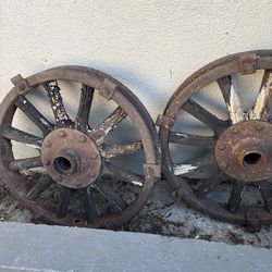 Two rustic, timeworn wagon wheels with corroded iron rims and sun-bleached wooden spokes