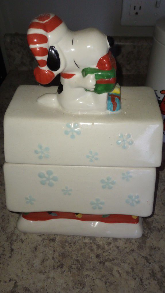 Peanuts Snoopy

Snowflakes Snowed Snow Ceramic Dog House white, Red, green, yellow blue Big Christmas Cookie Jar

Snoopy is wearing a Santa hat and so