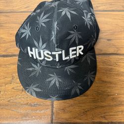 A black Hustler brand snapback hat featuring a leaf pattern and white embroidered logo Smoke free home