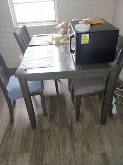 A small dining table with three chairs made out of wood and each chair is upholstered