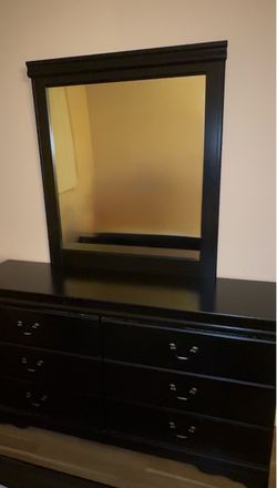 Black wooden bedroom dresser with an attached framed mirror with minor scratches.