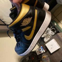 Nike Air Jordan 1 Mid in the black, white, and metallic gold colorway