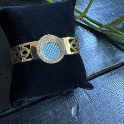 Gold bracelet with detail on cuff, circular blue and rhinestone pendant. 