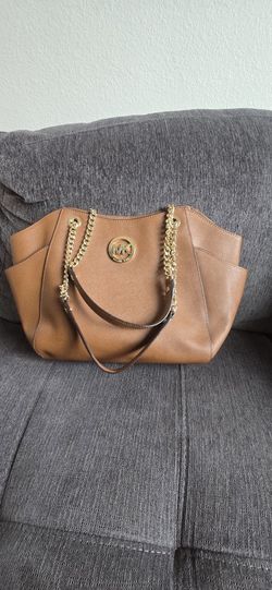 Stylish Michael Kors tote bag is made of brown saffiano leather. It has gold-tone chain and leather shoulder straps. Interior is lined with signature 