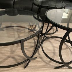 Set of three glass top tables with black metal frames.