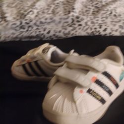 This is a pair of Kevin Lyons x adidas Superstar Infant 'Create Your Future' shoes in white and black. 