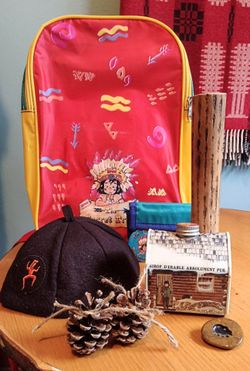 Lot of vintage novelty camping items: backpack, rain stick, brownie hat, stone, cabin syrup.