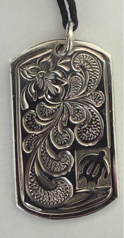 This silver Hawaiian tag pendant features an intricate scrollwork and plumeria flower design alongside a small sea turtle (honu) accent.