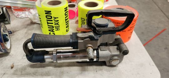 Heavy-duty hand-held pneumatic strapping machine for PET/PP plastic strapping. Connects to an air compressor and tensions, seals, and cuts plastic str
