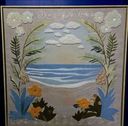 Embroidered textile artwork, from the 1970s, features a detailed seascape framed by tropical foliage. 24"×24"