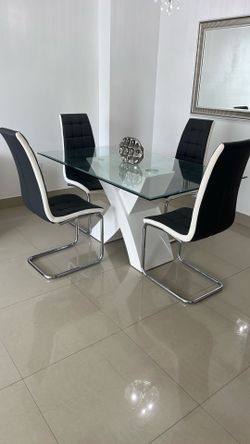 Modern glass dining table with four cushioned chairs.