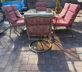 Set of 7Pcs, outdoor patio dining set featuring a glass-topped rectangular metal table and matching high-back chairs with red cushions.