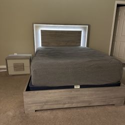 Modern bedroom set in excellent condition. Includes queen-size bed frame with LED-lit headboard, matching nightstand, and tall dresser.