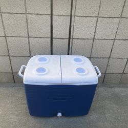 Rubbermaid blue 60-quart wheeled cooler with a split lid and a telescoping handle.