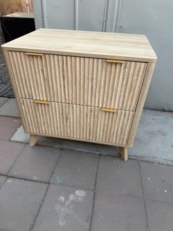 Light oak-finished wood file cabinet with two drawers. This piece has a fluted texture on the drawer fronts and gold-toned metal pull handles. It is s
