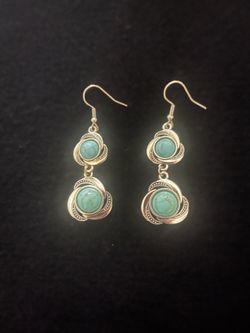 Elegant dangle earrings feature two tiers of turquoise-colored stones set in silver-tone metal. Each stone is encased in a decorative, swirling knot d