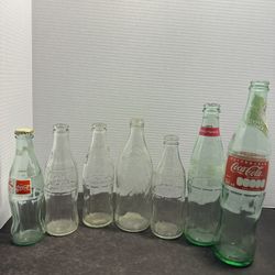 Lot of 7 vintage and collectible glass soda bottles featuring Coca-Cola and Pepsi-Cola. Includes several clear embossed Coke bottles, a Pepsi-Cola 16 