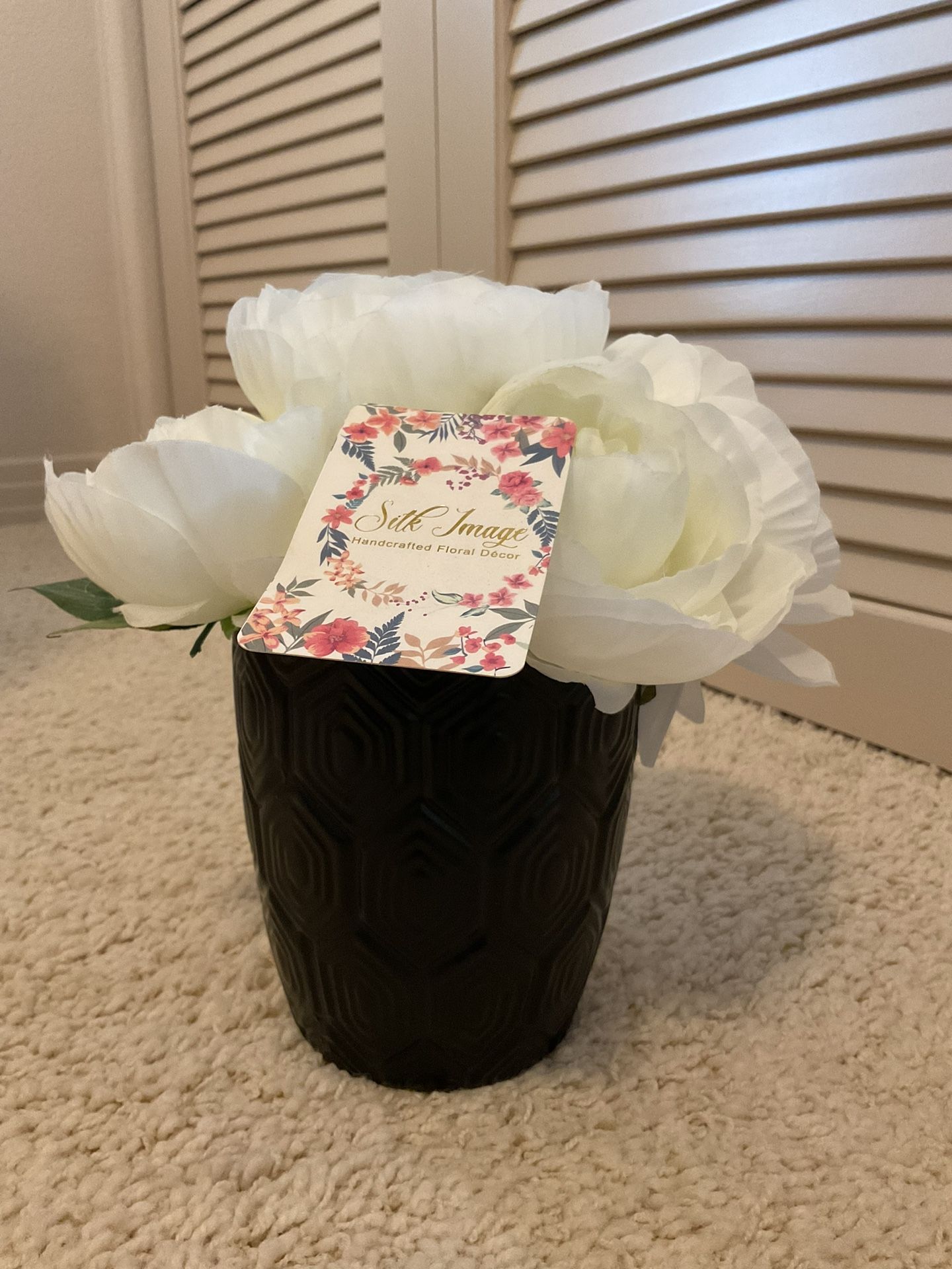 Elegant white artificial flowers in a textured black vase.