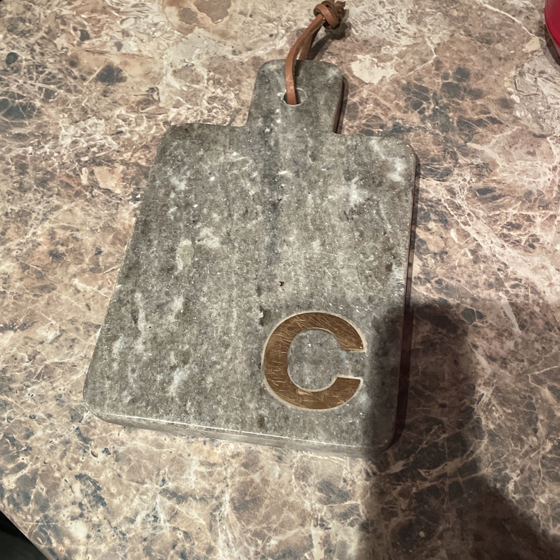 A Marble Small Cutting Board With Engraved Gold “C” On It