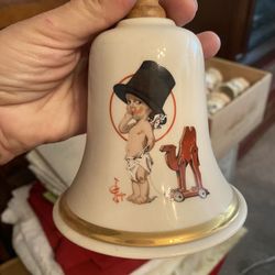 a 1977 Kewpie First Edition Annual Saturday Evening Post Bell. It is made of porcelain and features a Kewpie character, based on illustrations by Rose