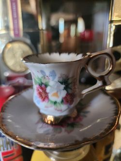 vintage footed demitasse teacup and saucer set features a hand-painted floral design with pink and white roses and delicate gold-rimmed edges.