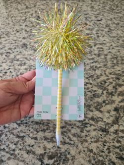 Yoobi pom pom pen with iridescent tinsel topper and a yellow-and-white checkered barrel, black ink