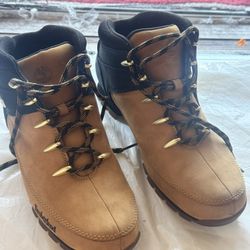 Timberland branded leather boots. Two-tone design with black upper and wheat brown panels. Gold-tone logo plaque detail. Contrasting laces add visual 