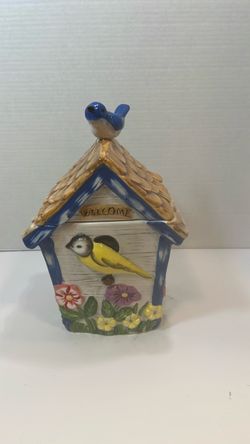 a ceramic birdhouse-shaped cookie jar featuring a yellow bird, flowers, a blue roof, and a bluebird figurine on the lid