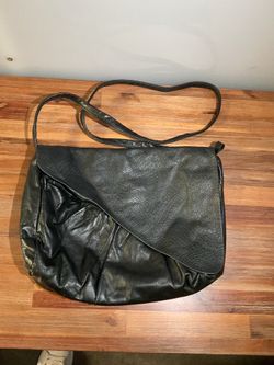 This black leather crossbody bag features a distinctive fold-over flap with a snakeskin-like texture.