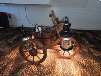 A rustic wooden chandelier inspired by a traditional wagon, featuring black metal lanterns. Its unique design, reminiscent of vintage wagons, adds an 