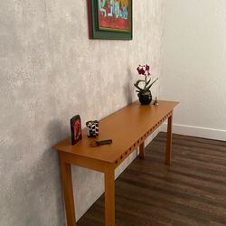 For sale pre-owned a slender and rectangular solid light oak wood  console table with a decorative perforated skirt along the apron.