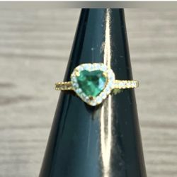 Delicate gold ring featuring a heart-shaped emerald-colored center stone. Sparkling pavé halo and band add refined shine. Perfect for everyday eleganc