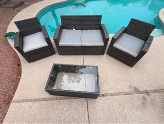 Juskys 4-piece PE wicker patio set features a black finish and iron-gray cushions. 4-piece set includes a loveseat, two chairs, and a glass-top table.
