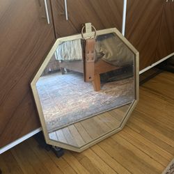 octagonal wall mirror with a gold-toned frame and a decorative leather hanging strap