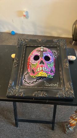 This is a hand-painted ceramic sugar skull calavera in a picture frame