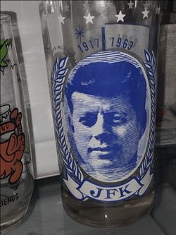This vintage 1963 John F. Kennedy memorial drinking glass features a blue portrait of the president framed by laurel wreaths and topped with stars.