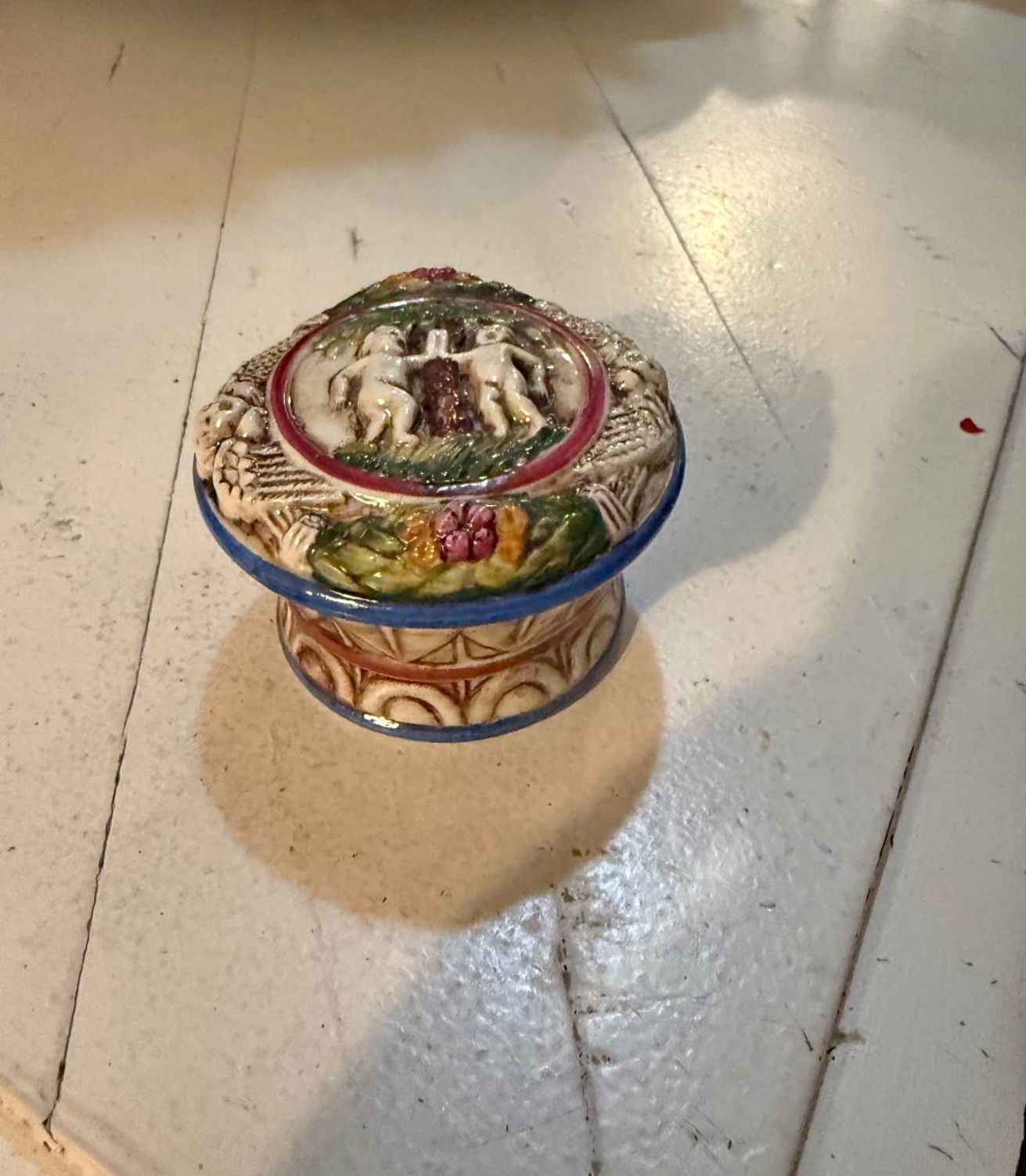 This is a vintage porcelain trinket box, possibly of German origin, featuring a raised design with figures and floral motifs.