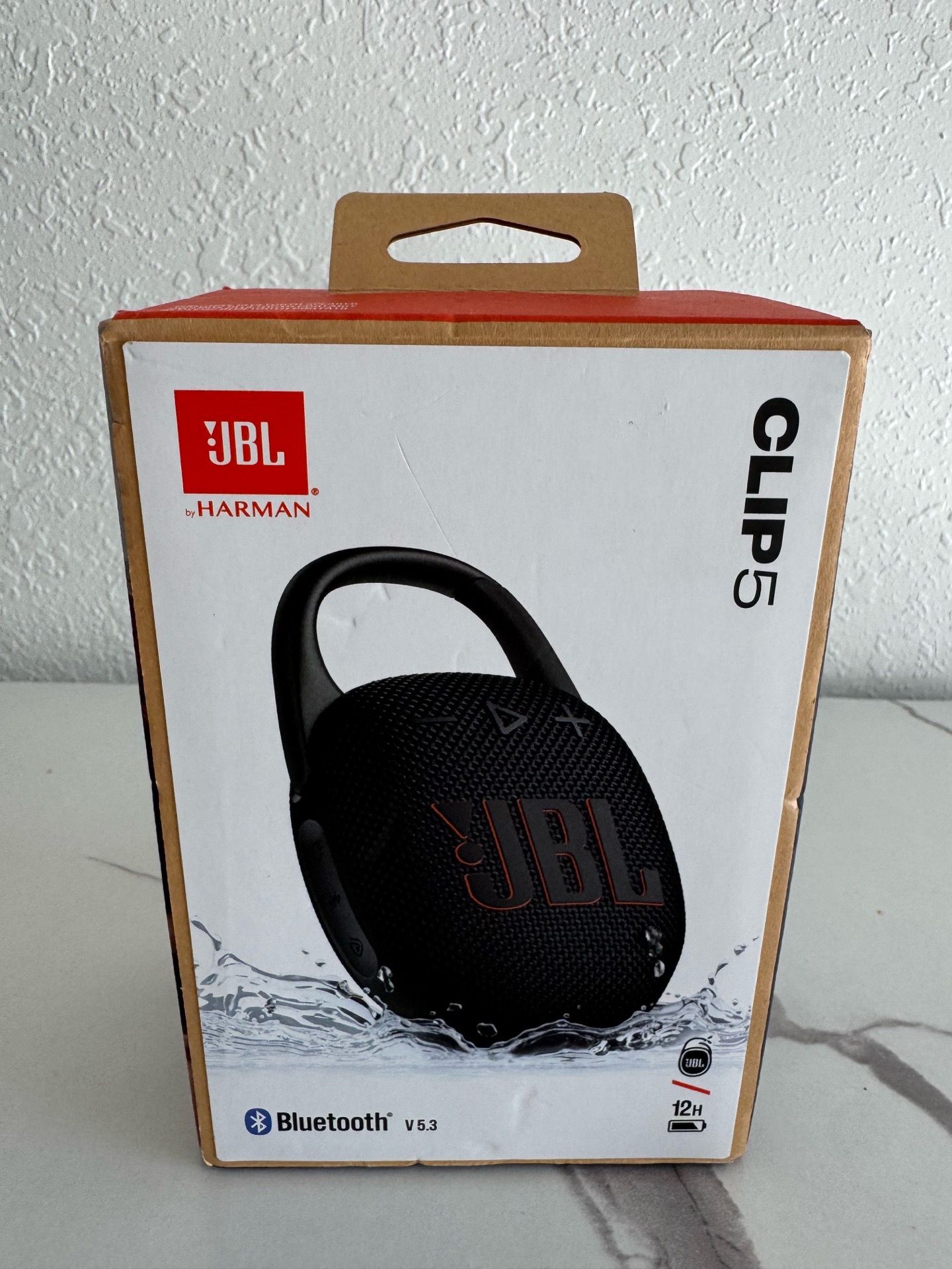 New JBL Clip 5 portable Bluetooth speaker. Speaker is black color. Has Bluetooth V5.3, IP67 waterproof and dustproof. Provides up to 12 hours playtime