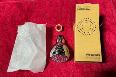 chrome-finished Wassa high-pressure shower head next to its packaging box, protective wrapping, and a rubber washer/flow