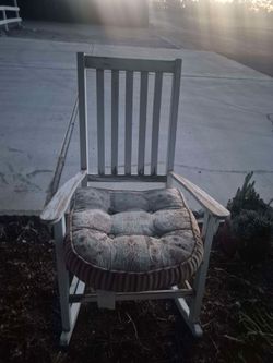 white wooden rocking chair featuring a worn, slatted back design and a patterned, plush cushion.
