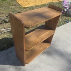 That is a Mid-Century Modern (MCM) wooden bookshelf or record rack, likely from the 1950s or 1960s. Its sleek, rounded edges and "floating" shelf look