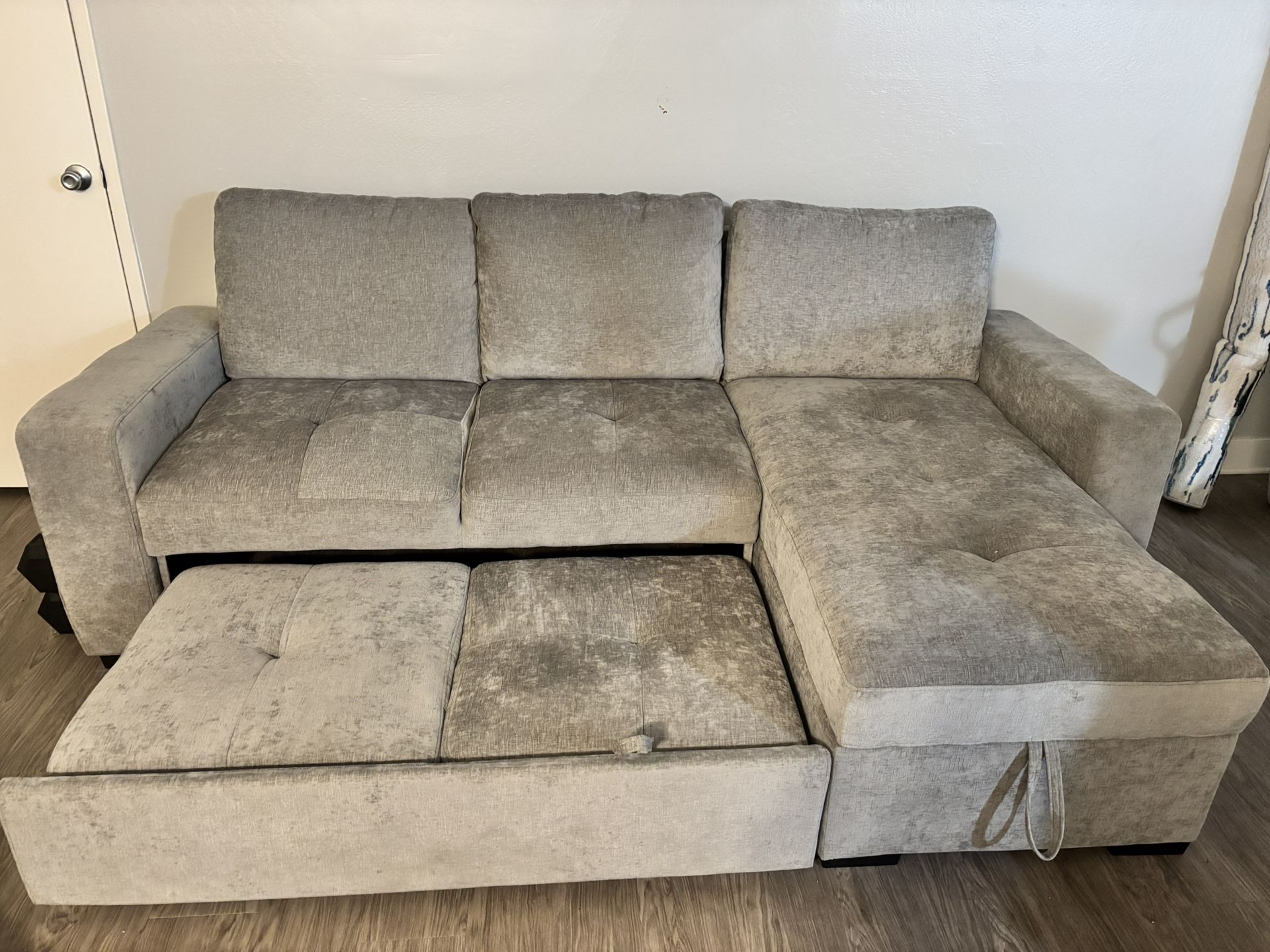Light gray sectional couch with right-side chaise. Chaise has hidden storage and the main cushions pull out for a sleeper-style bed. Middle backrest f