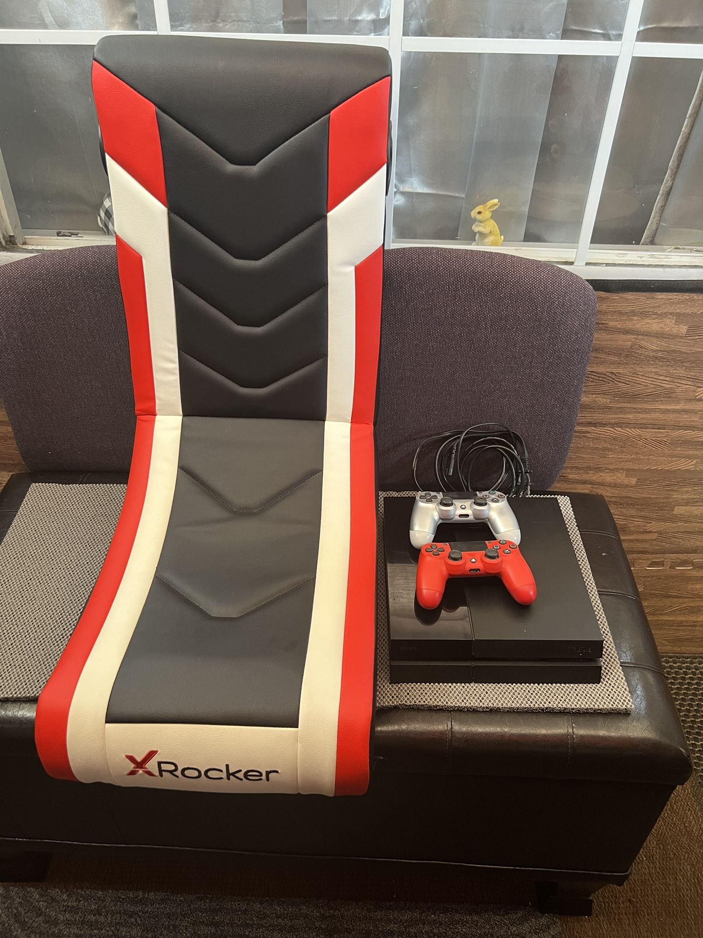 Sony PlayStation 4 console, likely the Slim model, along with two DualShock 4 wireless controllers, one red and one silver.