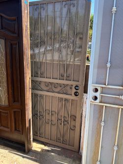 Durable wrought iron security screen door in a tan finish. This door has decorative scrollwork patterns and a perforated metal screen for ventilation