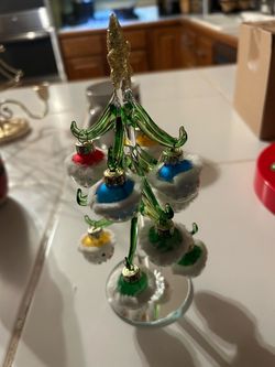hand-crafted green blown-glass miniature Christmas tree decorated with small colorful glass ball ornaments wearing white fuzzy trim (such as those mad