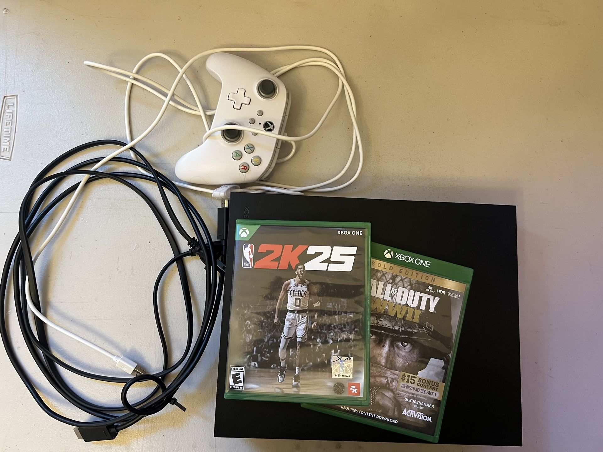 Xbox One X 1TB console for sale, comes with two games—Call of Duty: WWII and NBA 2K25—and a white wired controller. Available in Lindsay for $110
