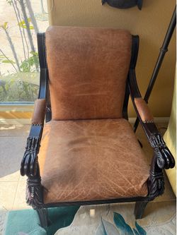 Brown leather armchair and ottoman with intricately carved dark wood frames.