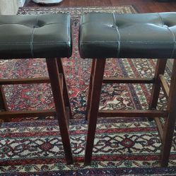 A Set Of Bar Stools. Dark Colored Wood And Black Pleather Seat Cushions