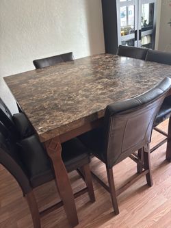 counter-height dining table set with a faux marble top, dark wood base, and 8 padded black faux leather chairs.